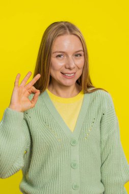 - Tamam. Neşeli, orta yaşlı, orta yaşlı bir kadın kameraya bakıp olumlu geri bildirim imzalar, güzel bir şeyi onaylar, zaferi kutlar gibi iyi hareketlerde bulunur. Sarı arka planda yetişkin bir kız.