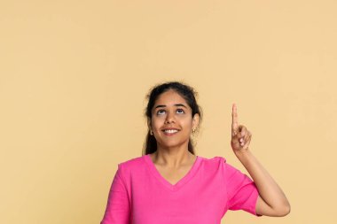 Hintli kadın parmağını yukarı kaldırarak önemli bir mesaj ya da yukarıdaki duyuruyu işaret ediyor. Bej arka plandaki kız önemi vurguluyor, dikkat çekiyor, önceliği vurguluyor, ciddiyet, tetikte olma