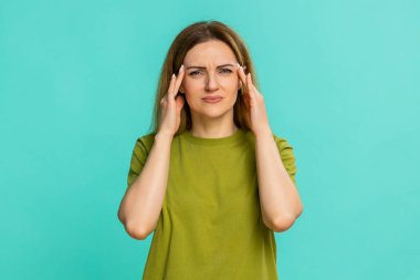 Orta yaşlı bir kadın kafasını tutuyor ve şakaklarına rahatsızlık veriyor. Migren veya baş ağrısı belirtileri gösteriyor. Mavi arka planda izole edilmiş bir kız stres, gerilim ve fiziksel rahatsızlık gösterir.