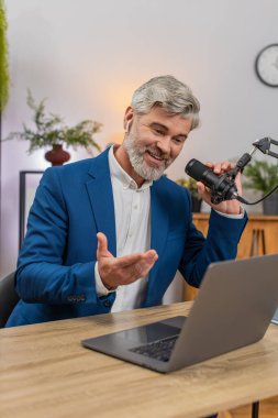 Merkez ofisteki orta yaşlı işadamı canlı jestler kullanarak podcast 'i stüdyo mikrofonuna aktarıyor. Masadaki serbest çalışan adam soruları cevaplıyor. Ses tonunu neşeli dinleyiciler canlı tutuyor..