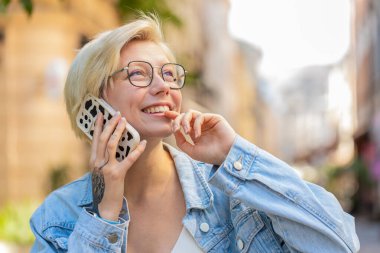 Telefon, iyi haber, dedikodu. Akıllı telefonda hoş sohbetler yapan mutlu beyaz kadın dışarıda arkadaşlarıyla konuşmaktan zevk alıyor. Şehir caddesinde modaya uygun giyinmiş bir kız. Kasaba yaşam tarzları.