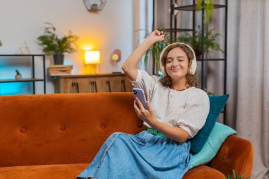 Kablosuz kulaklıklarla mutlu genç bir kadın evinde koltukta oturup en sevdiği enerjik disko dans müziğini dinliyor. İnsanlar hafta sonları boş zaman aktiviteleri yapar. Yaşam Tarzları