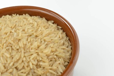 Beyaz arka planda bir kasede çiğ kahverengi pirinç.