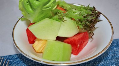 watermelon, melon, papaya and lettuce on a white plate
