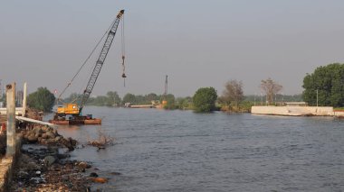 Nehrin ağzında ağır ekipmanlarla beton baraj inşaatı var.