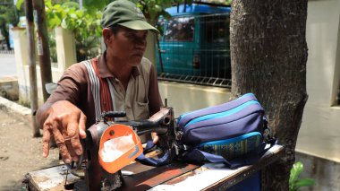 Sokak terzisi, Pekalongan Endonezya 6 Şubat 2024 'te manuel dikiş makinesiyle sipariş onarım çantası hazırlıyor.