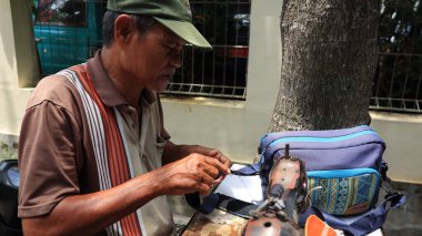 Sokak terzisi, Pekalongan Endonezya 6 Şubat 2024 'te manuel dikiş makinesiyle sipariş onarım çantası hazırlıyor.