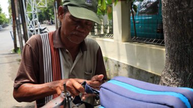 Sokak terzisi, Pekalongan Endonezya 6 Şubat 2024 'te manuel dikiş makinesiyle sipariş onarım çantası hazırlıyor.