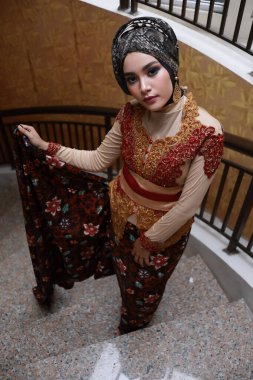 Güzel görünümlü Endonezyalı kadın tesettür takıyor ve Kebaya güzel bir batik kumaşa sarılmış.