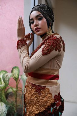 Güzel görünümlü Endonezyalı kadın tesettür takıyor ve Kebaya güzel bir batik kumaşa sarılmış.