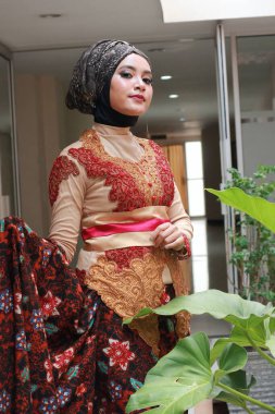 Güzel görünümlü Endonezyalı kadın tesettür takıyor ve Kebaya güzel bir batik kumaşa sarılmış.