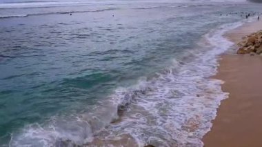 Dalgalar çarpıyor, güneşli bir gün. Kumsal ve tepeler boyunca büyük malikaneler. İnsanlar dinleniyor, oynuyor ve yüzüyor.