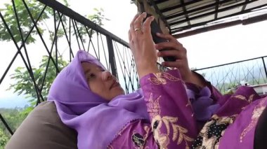 Evinin terasında uzanırken akıllı telefonuyla oynayan Asyalı bir kadın.