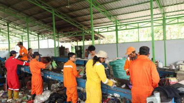 3 Haziran 2025 'te Pekalongan Endonezya' da, geri dönüşümlü materyalleri sınıflandırmak için atık işleme fabrikasında çalışırken güvenlik kıyafeti ve kask giyen işçilerin portresi