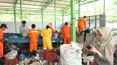 3 Haziran 2025 'te Pekalongan Endonezya' da, geri dönüşümlü materyalleri sınıflandırmak için atık işleme fabrikasında çalışırken güvenlik kıyafeti ve kask giyen işçilerin portresi