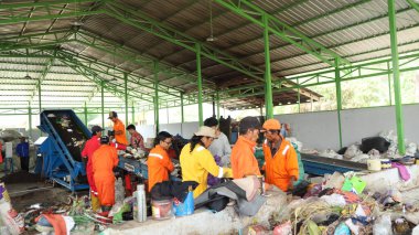 3 Haziran 2025 'te Pekalongan Endonezya' da, geri dönüşümlü materyalleri sınıflandırmak için atık işleme fabrikasında çalışırken güvenlik kıyafeti ve kask giyen işçilerin portresi