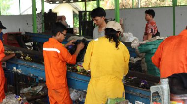 3 Haziran 2025 'te Pekalongan Endonezya' da, geri dönüşümlü materyalleri sınıflandırmak için atık işleme fabrikasında çalışırken güvenlik kıyafeti ve kask giyen işçilerin portresi