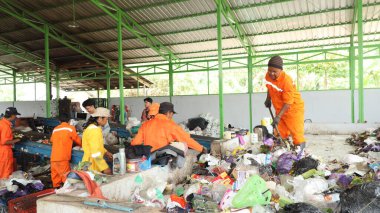 3 Haziran 2025 'te Pekalongan Endonezya' da, geri dönüşümlü materyalleri sınıflandırmak için atık işleme fabrikasında çalışırken güvenlik kıyafeti ve kask giyen işçilerin portresi