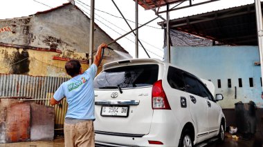 Pekalongan, Endonezya 'da geleneksel bir araba yıkamada yüksek basınçlı su hortumuyla beyaz bir Toyota Avanza' yı temizleyen yaşlı bir adam. 4 Haziran 2025.