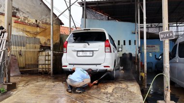 Pekalongan, Endonezya 'da geleneksel bir araba yıkamada yüksek basınçlı su hortumuyla beyaz bir Toyota Avanza' yı temizleyen yaşlı bir adam. 4 Haziran 2025.