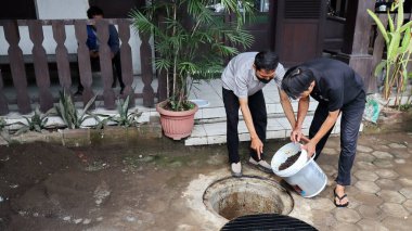 Temizlik işçisi organik mutfak atıklarını açık hava gübre çukuruna atıyor. Sahne, Pekalongan Endonezya kentsel ortamında sürdürülebilir atık yönetimi ve çevre dostu uygulamaları yakalıyor, 13 Mayıs 2025