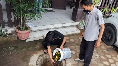 Temizlik işçisi organik mutfak atıklarını açık hava gübre çukuruna atıyor. Sahne, Pekalongan Endonezya kentsel ortamında sürdürülebilir atık yönetimi ve çevre dostu uygulamaları yakalıyor, 13 Mayıs 2025