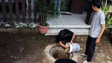 Temizlik işçisi organik mutfak atıklarını açık hava gübre çukuruna atıyor. Sahne, Pekalongan Endonezya kentsel ortamında sürdürülebilir atık yönetimi ve çevre dostu uygulamaları yakalıyor, 13 Mayıs 2025