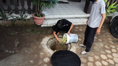 Temizlik işçisi organik mutfak atıklarını açık hava gübre çukuruna atıyor. Sahne, Pekalongan Endonezya kentsel ortamında sürdürülebilir atık yönetimi ve çevre dostu uygulamaları yakalıyor, 13 Mayıs 2025
