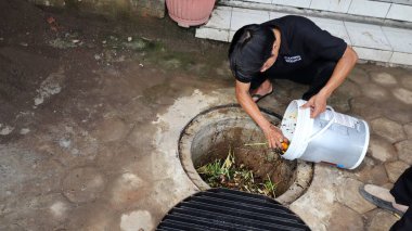 Temizlik işçisi organik mutfak atıklarını açık hava gübre çukuruna atıyor. Sahne, Pekalongan Endonezya kentsel ortamında sürdürülebilir atık yönetimi ve çevre dostu uygulamaları yakalıyor, 13 Mayıs 2025