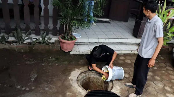 Temizlik işçisi organik mutfak atıklarını açık hava gübre çukuruna atıyor. Sahne, Pekalongan Endonezya kentsel ortamında sürdürülebilir atık yönetimi ve çevre dostu uygulamaları yakalıyor, 13 Mayıs 2025