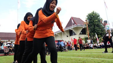 Şenlikli kalabalık ve ulusal gururla heyecanlı bir takım oyunu. Erkekler, Endonezya Bağımsızlık Günü kutlamaları sırasında 14 Ağustos 2025 'te Pekalongan, Orta Java' da geleneksel bir bakiak yarışında yarışıyorlar..