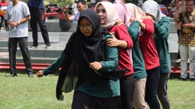 Şenlikli kalabalık ve ulusal gururla heyecanlı bir takım oyunu. Erkekler, Endonezya Bağımsızlık Günü kutlamaları sırasında 14 Ağustos 2025 'te Pekalongan, Orta Java' da geleneksel bir bakiak yarışında yarışıyorlar..