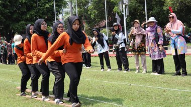 Şenlikli kalabalık ve ulusal gururla heyecanlı bir takım oyunu. Erkekler, Endonezya Bağımsızlık Günü kutlamaları sırasında 14 Ağustos 2025 'te Pekalongan, Orta Java' da geleneksel bir bakiak yarışında yarışıyorlar..