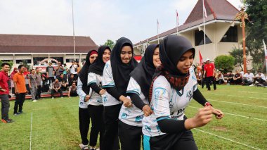 Şenlikli kalabalık ve ulusal gururla heyecanlı bir takım oyunu. Erkekler, Endonezya Bağımsızlık Günü kutlamaları sırasında 14 Ağustos 2025 'te Pekalongan, Orta Java' da geleneksel bir bakiak yarışında yarışıyorlar..