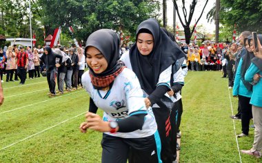 Şenlikli kalabalık ve ulusal gururla heyecanlı bir takım oyunu. Erkekler, Endonezya Bağımsızlık Günü kutlamaları sırasında 14 Ağustos 2025 'te Pekalongan, Orta Java' da geleneksel bir bakiak yarışında yarışıyorlar..