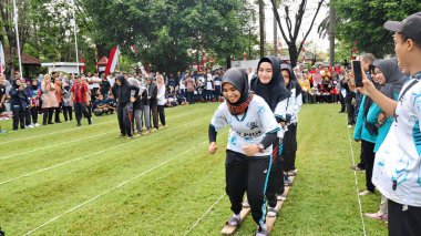 Şenlikli kalabalık ve ulusal gururla heyecanlı bir takım oyunu. Erkekler, Endonezya Bağımsızlık Günü kutlamaları sırasında 14 Ağustos 2025 'te Pekalongan, Orta Java' da geleneksel bir bakiak yarışında yarışıyorlar..