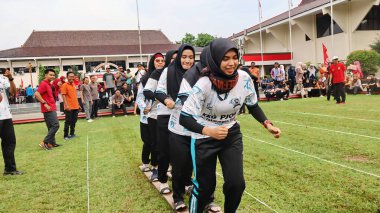 Şenlikli kalabalık ve ulusal gururla heyecanlı bir takım oyunu. Erkekler, Endonezya Bağımsızlık Günü kutlamaları sırasında 14 Ağustos 2025 'te Pekalongan, Orta Java' da geleneksel bir bakiak yarışında yarışıyorlar..