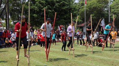 Şenlikli kalabalık ve ulusal gururla heyecanlı bir takım oyunu. Erkekler, Endonezya Bağımsızlık Günü kutlamaları sırasında 14 Ağustos 2025 'te Pekalongan, Orta Java' da geleneksel bir bakiak yarışında yarışıyorlar..
