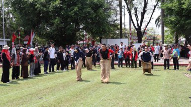 Şenlikli kalabalık ve ulusal gururla heyecanlı bir takım oyunu. Erkekler, Endonezya Bağımsızlık Günü kutlamaları sırasında 14 Ağustos 2025 'te Pekalongan, Orta Java' da geleneksel bir bakiak yarışında yarışıyorlar..