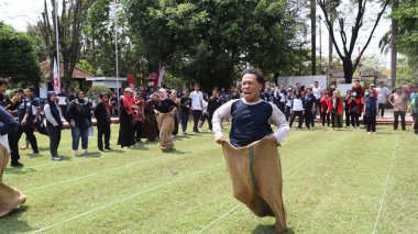Şenlikli kalabalık ve ulusal gururla heyecanlı bir takım oyunu. Erkekler, Endonezya Bağımsızlık Günü kutlamaları sırasında 14 Ağustos 2025 'te Pekalongan, Orta Java' da geleneksel bir bakiak yarışında yarışıyorlar..