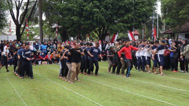 Şenlikli kalabalık ve ulusal gururla heyecanlı bir takım oyunu. Erkekler, Endonezya Bağımsızlık Günü kutlamaları sırasında 14 Ağustos 2025 'te Pekalongan, Orta Java' da geleneksel bir bakiak yarışında yarışıyorlar..