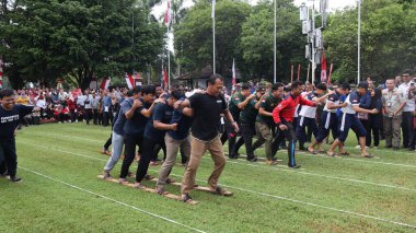 Şenlikli kalabalık ve ulusal gururla heyecanlı bir takım oyunu. Erkekler, Endonezya Bağımsızlık Günü kutlamaları sırasında 14 Ağustos 2025 'te Pekalongan, Orta Java' da geleneksel bir bakiak yarışında yarışıyorlar..
