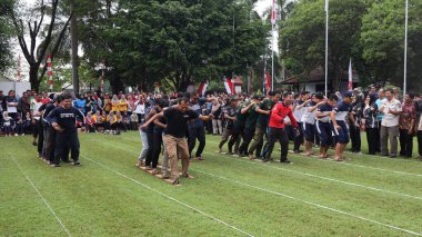 Şenlikli kalabalık ve ulusal gururla heyecanlı bir takım oyunu. Erkekler, Endonezya Bağımsızlık Günü kutlamaları sırasında 14 Ağustos 2025 'te Pekalongan, Orta Java' da geleneksel bir bakiak yarışında yarışıyorlar..
