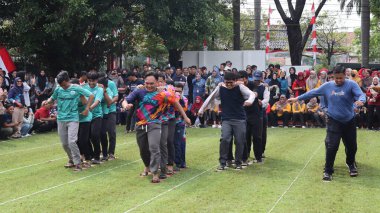 Şenlikli kalabalık ve ulusal gururla heyecanlı bir takım oyunu. Erkekler, Endonezya Bağımsızlık Günü kutlamaları sırasında 14 Ağustos 2025 'te Pekalongan, Orta Java' da geleneksel bir bakiak yarışında yarışıyorlar..