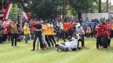 Şenlikli kalabalık ve ulusal gururla heyecanlı bir takım oyunu. Erkekler, Endonezya Bağımsızlık Günü kutlamaları sırasında 14 Ağustos 2025 'te Pekalongan, Orta Java' da geleneksel bir bakiak yarışında yarışıyorlar..