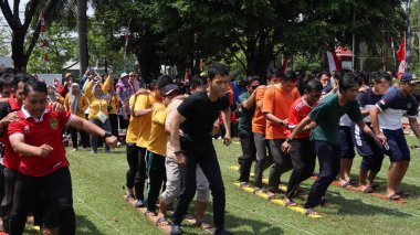 Şenlikli kalabalık ve ulusal gururla heyecanlı bir takım oyunu. Erkekler, Endonezya Bağımsızlık Günü kutlamaları sırasında 14 Ağustos 2025 'te Pekalongan, Orta Java' da geleneksel bir bakiak yarışında yarışıyorlar..