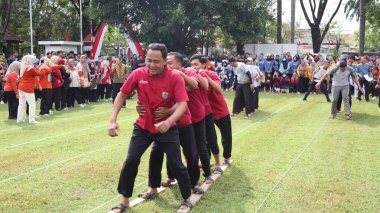 Şenlikli kalabalık ve ulusal gururla heyecanlı bir takım oyunu. Erkekler, Endonezya Bağımsızlık Günü kutlamaları sırasında 14 Ağustos 2025 'te Pekalongan, Orta Java' da geleneksel bir bakiak yarışında yarışıyorlar..