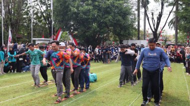 Şenlikli kalabalık ve ulusal gururla heyecanlı bir takım oyunu. Erkekler, Endonezya Bağımsızlık Günü kutlamaları sırasında 14 Ağustos 2025 'te Pekalongan, Orta Java' da geleneksel bir bakiak yarışında yarışıyorlar..