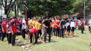 Şenlikli kalabalık ve ulusal gururla heyecanlı bir takım oyunu. Erkekler, Endonezya Bağımsızlık Günü kutlamaları sırasında 14 Ağustos 2025 'te Pekalongan, Orta Java' da geleneksel bir bakiak yarışında yarışıyorlar..