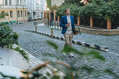 Gülümseyen yakışıklı iş adamı. Takım elbiseli. Elinde kahve ve uzun tahta bir sokak var.